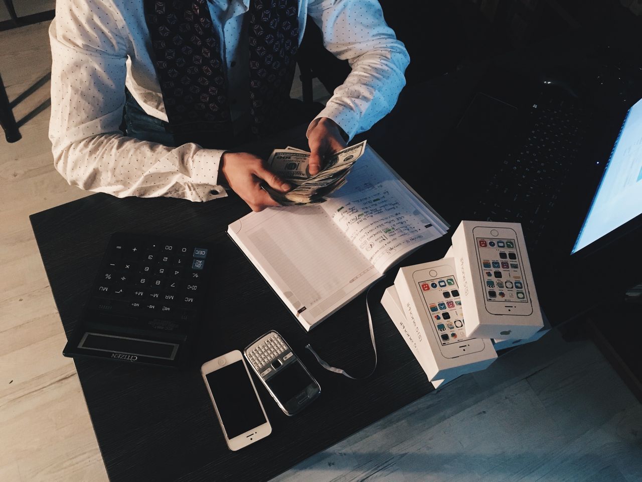 about-us-02 Businessman organizing finances with tech devices and cash on desk.