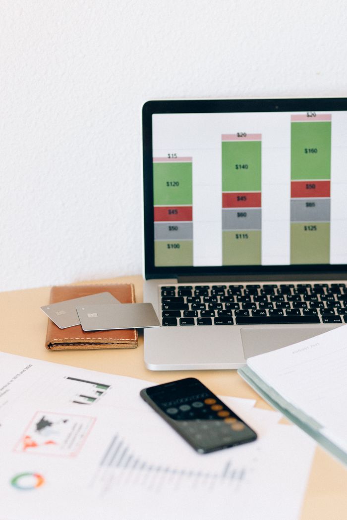 about-us-01 Laptop displaying financial chart alongside documents and credit cards on desk.